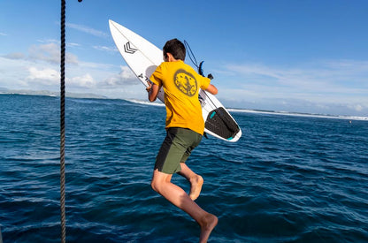 Kai Queenan jumping off boat into ocean with surfboard wearing the Mad Otter T-Shirt